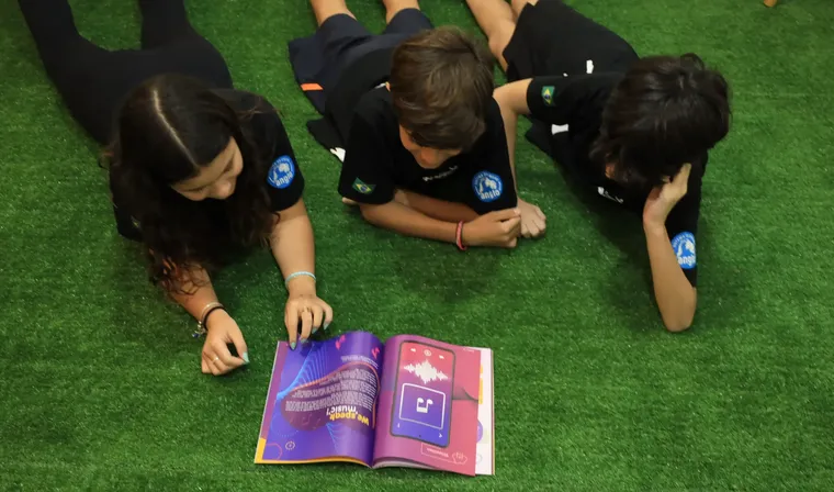 Alunos lendo o material bilíngue do Criarte no gramado da escola